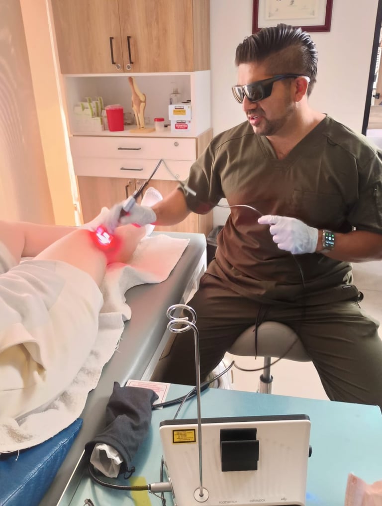Director Clínico de R4 Fisioterapia Regenerativa en scrubs oscuros realizando tratamiento con láser en la pierna de un paciente en entorno clínico profesional
