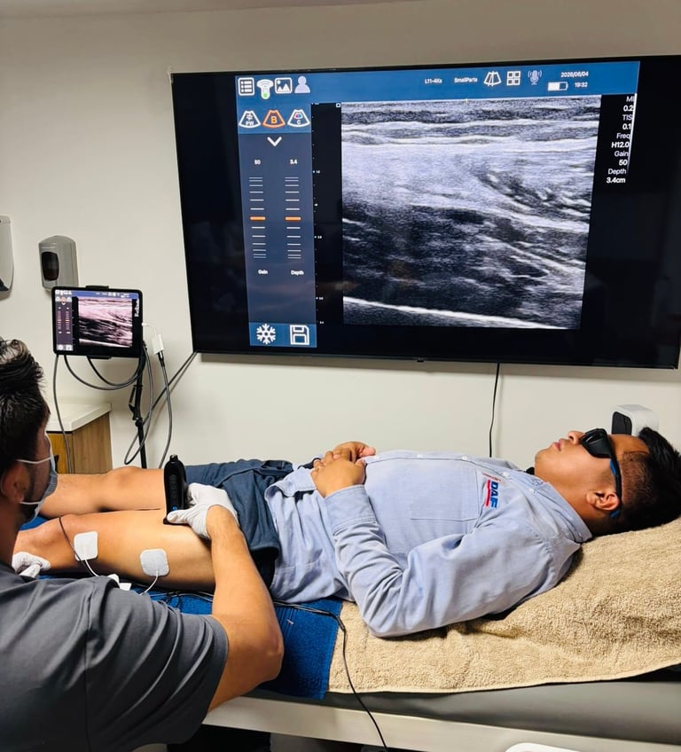 Director Clínico de R4 Fisioterapia Regenerativa realizando examen de ultrasonido a un paciente acostado en camilla mientras la imagen ecográfica se proyecta en un monitor de pared